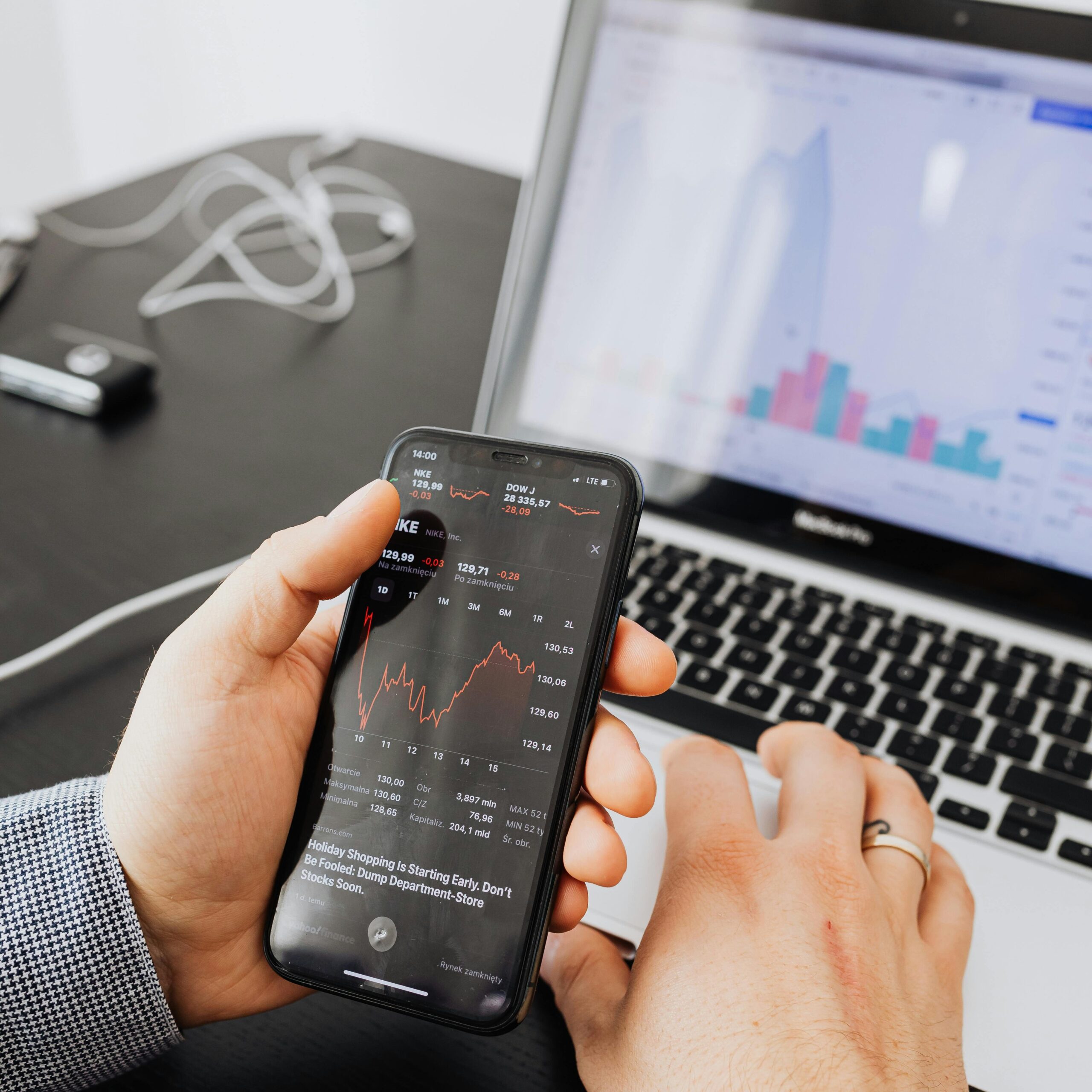 Hands holding smartphone analyzing stock market data next to laptop displaying charts.